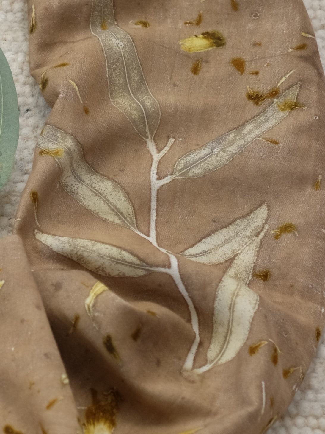 detail of an ecoprinted infinity scarf with a eucalyptus leave and marigold speckles.