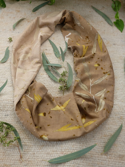 ecoprinted infnity scarf with a dark and a bright side. over a carpet with eucalyptus leaves around it.