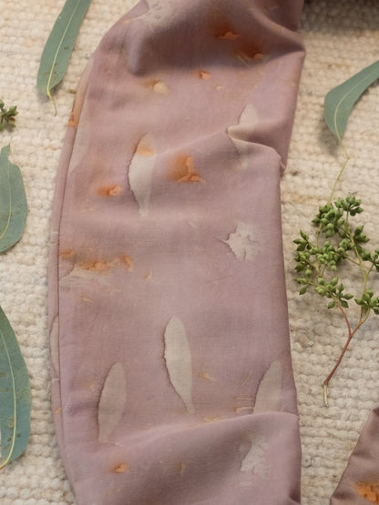 section of an ecoprinted scarf , in a grey purple color , surrounded with eucalyptus leaves.