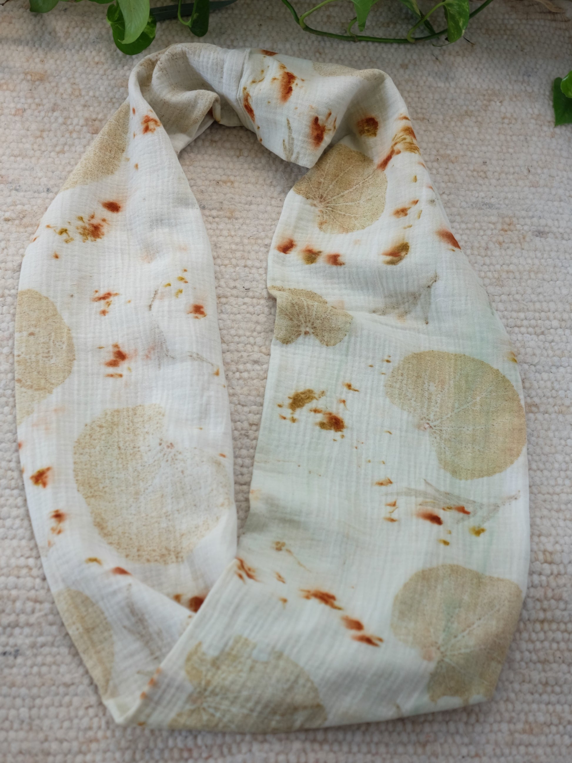 ecoprinted scarf, with judas tree leaves and cosmos flowers. the scarf is creme color with leaves in yellow and orange. layed over a white carpet.