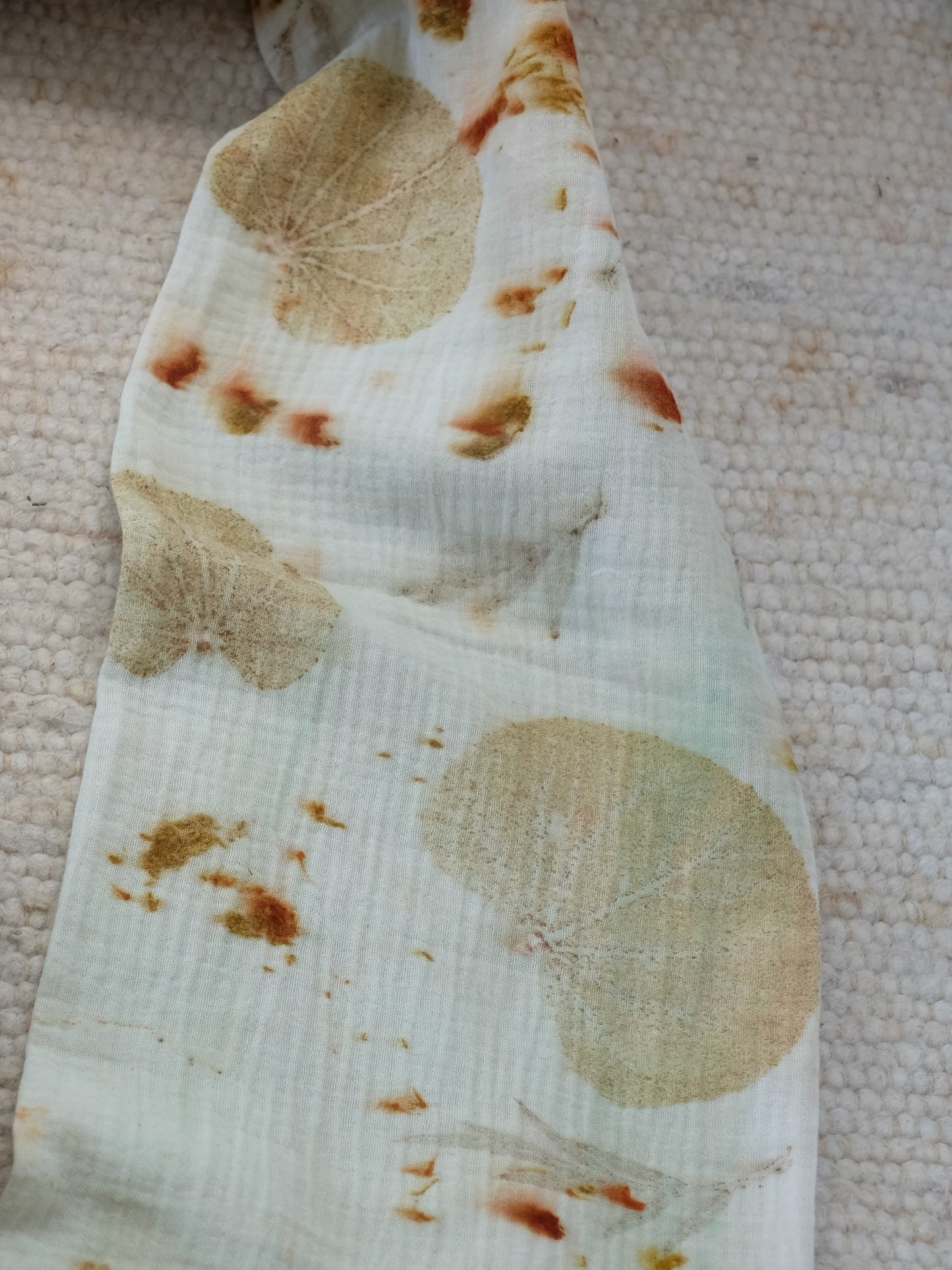 section of an ecoprinted scarf, in creme color and yellow leaves. with speckles of orange.