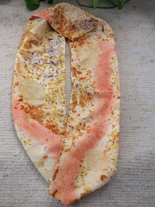 bundle dyed scarf , in pink, yellow, orange, khaki colors, layed over a white carpet.