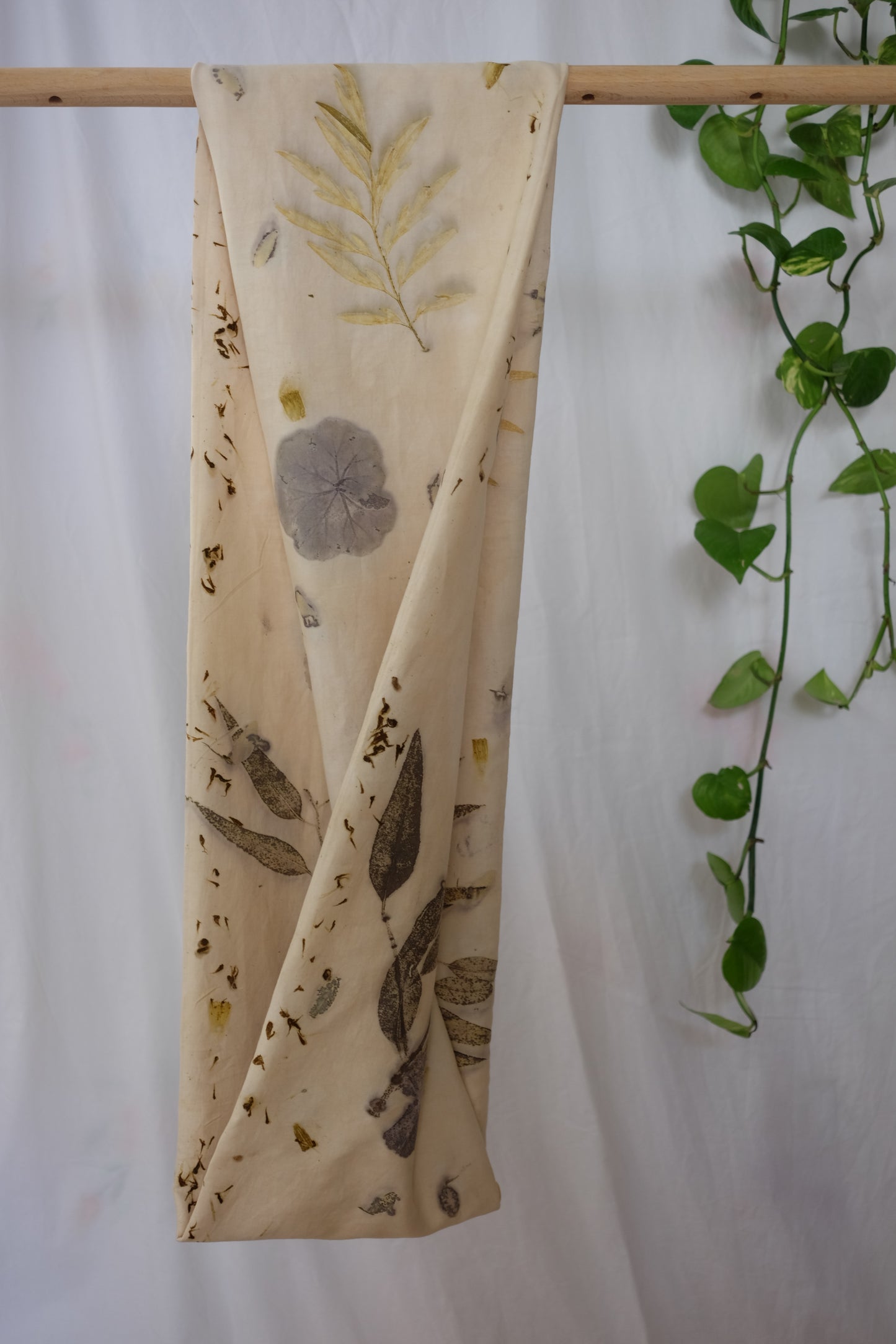 ecoprinted scarf, with leaves of eucalyptus and geranioum. pictured he folded side of the infinity scarf that is hanging on a dowel.
