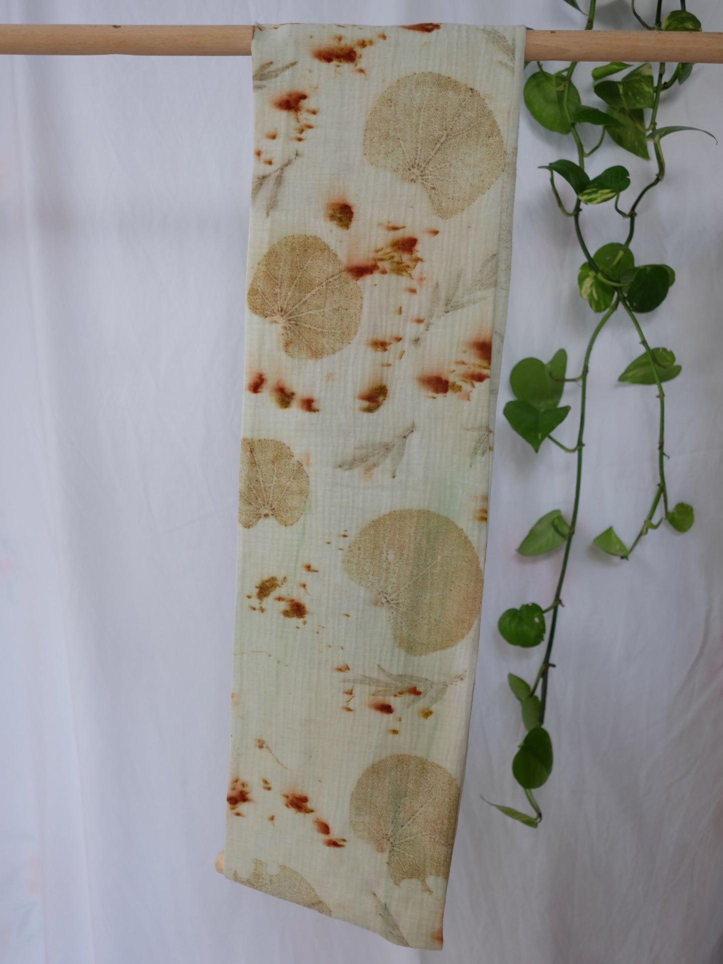 ecoprinted scarf hanging on a dowel with a white background and a pothos plant in the side.