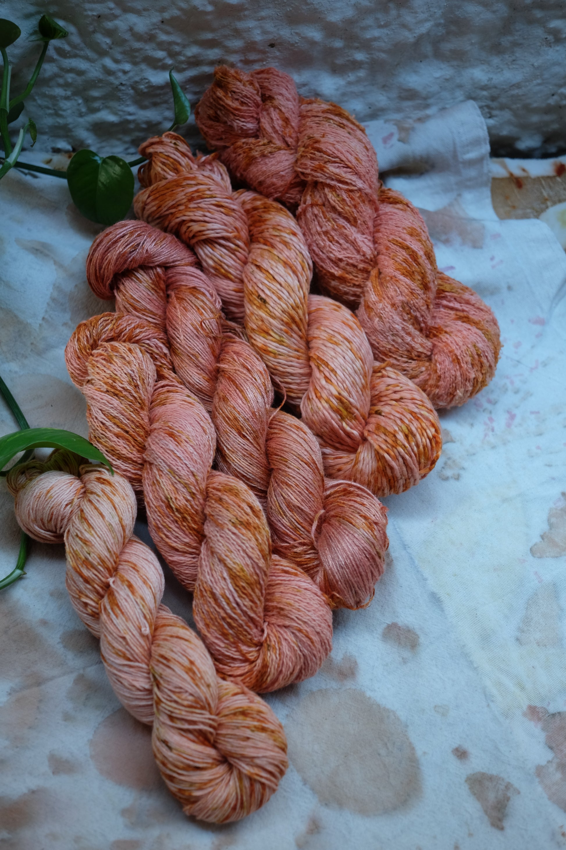 5 skeins of vegan yarn, botanically dyed in pink color, with range and yellow speckles. laying over an ecoprinted fabric.