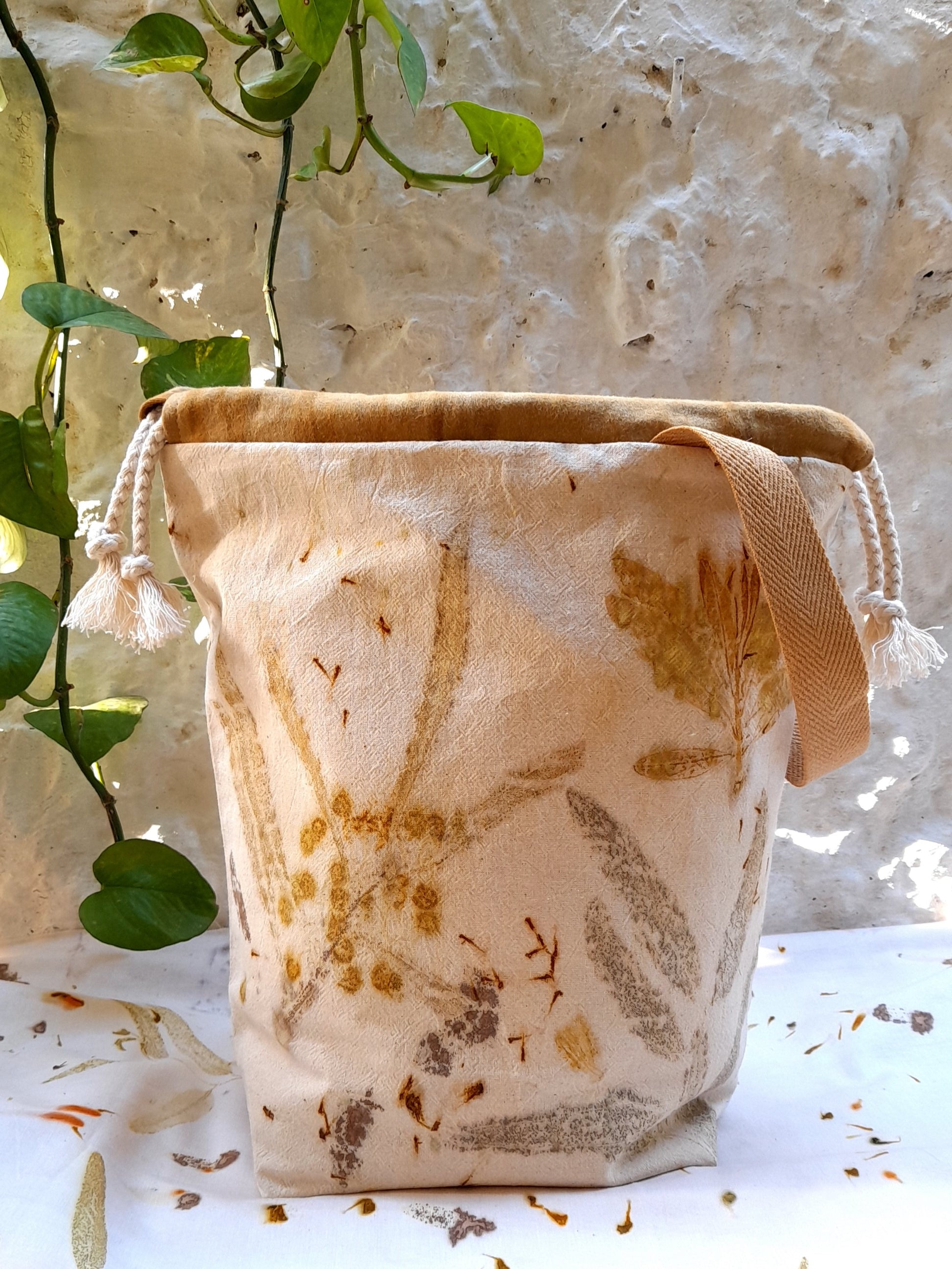 ecoprinted project bag, made with coton fabric in shades or yellow and brown. standing in front of a white wall and on top of a white table with small leaves print.