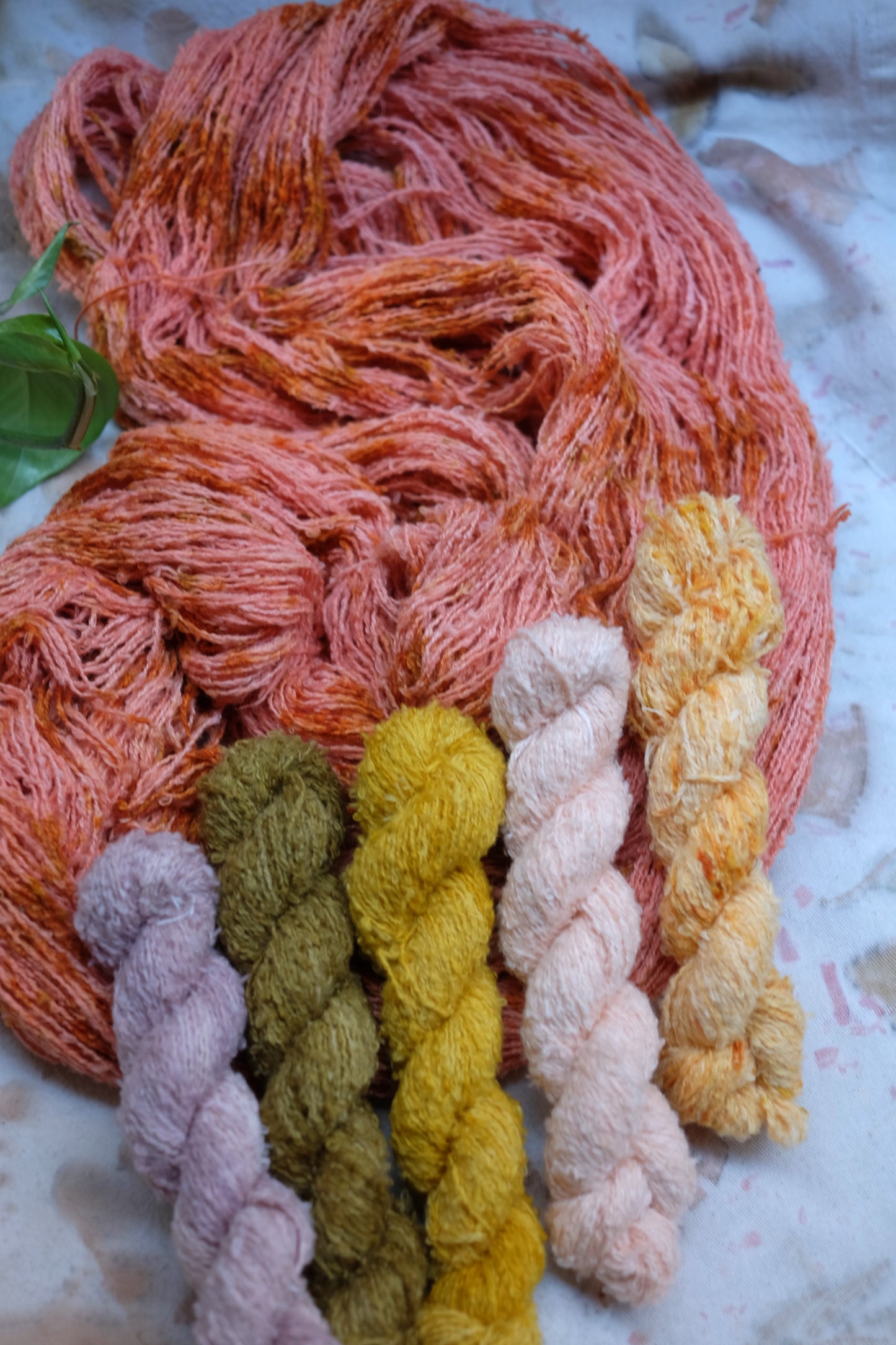 botanically dyed vegan yarn. one open skein of yarn in pink color with yellow and orange speckles, on top of the open skein, lay 5 mini skeins in the colors of lilac, green, yellow,pink and orange.